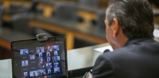 deputado julio garcia com um notebook na frente com transmissão de video dos deputados na tela