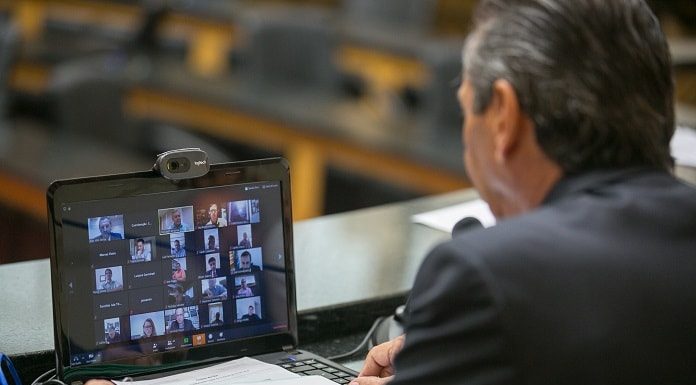 deputado julio garcia com um notebook na frente com transmissão de video dos deputados na tela