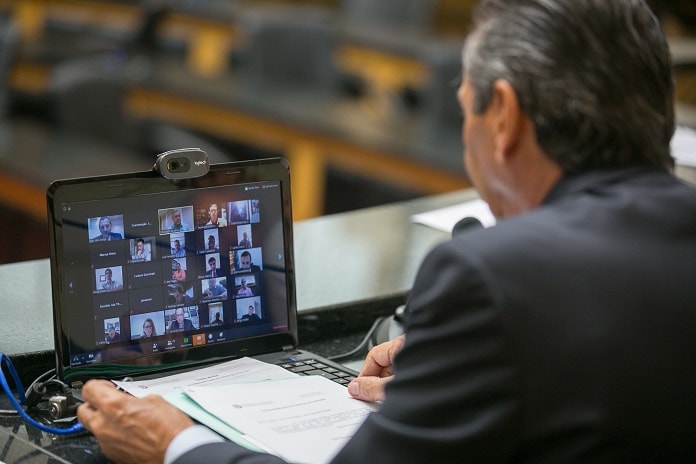 deputado julio garcia com um notebook na frente com transmissão de video dos deputados na tela