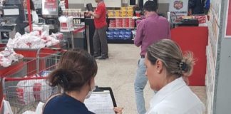 fiscal da vigilância mostra prancheta para mulher funcionária do supermercado, perto dos caixas