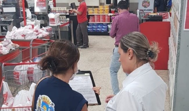 fiscal da vigilância mostra prancheta para mulher funcionária do supermercado, perto dos caixas
