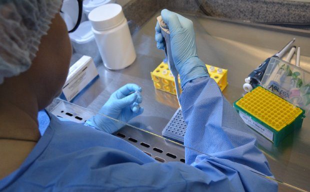 mulher usando diversos equipamentos de proteção opera teste de coronavírus sobre bancada com equipamentos de laboratório