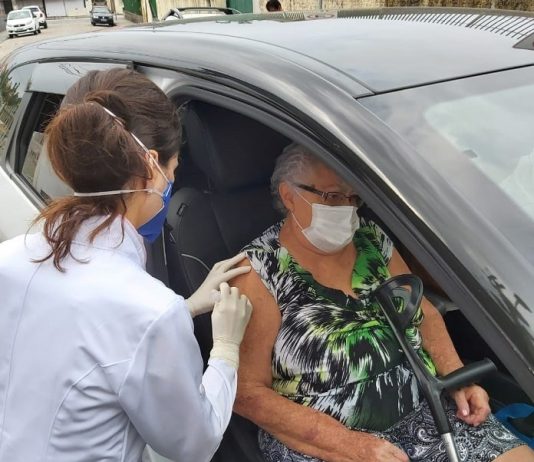 idosa dentro de carro recebendo vacina de uma profissional de saúde com jaleco
