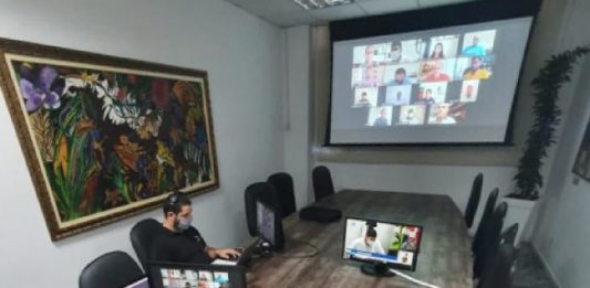 Vedada a nomeação em São José de condenados na Lei Maria da Penha presidente da cmsj sentado na ponta de uma mesa, com servidor ao lado, ambos em notebooks, ao fundo telão com outros vereadores