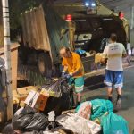 dois funcionários da comcap atrás de caminhão compactador estacionado na av. hercílio luz onde há pilha de lixo no calçadão