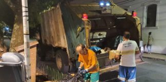 dois funcionários da comcap atrás de caminhão compactador estacionado na av. hercílio luz onde há pilha de lixo no calçadão