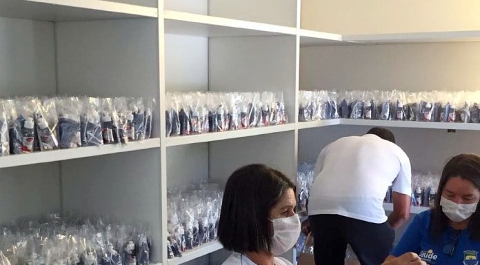 duas mulheres usando máscaras, sentadas,montando kits de proteção individual