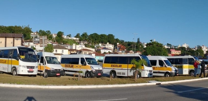 vans e micro-ônibus escolares estacionadas juntas ao lado da avenida beira-mar de sj; morro com casas ao fundo