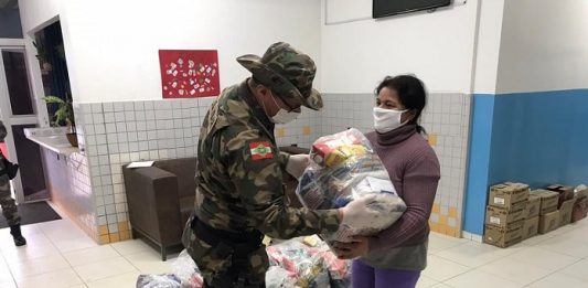 Doação de alimentos, plantio de mudas e nova farda nos 30 anos da PM Ambiental Policial militar entregando alimentos a uma senhora