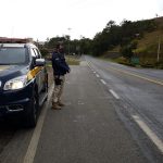 policial Rodoviário Federal de pé ao lado da viatura