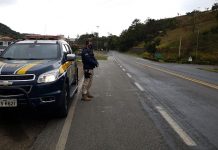 policial Rodoviário Federal de pé ao lado da viatura