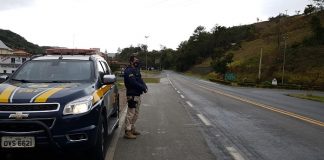 policial Rodoviário Federal de pé ao lado da viatura