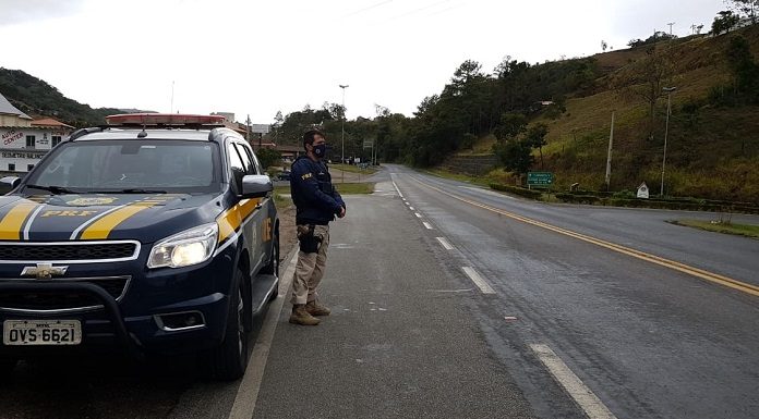 policial Rodoviário Federal de pé ao lado da viatura