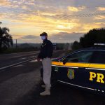 Policial Rodoviário de pé ao lado da viatura