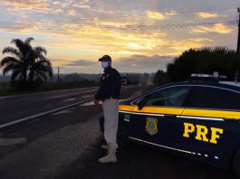 Policial Rodoviário de pé ao lado da viatura