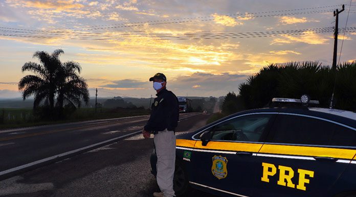 Policial Rodoviário de pé ao lado da viatura