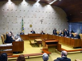 ministros do stf em reunião no plenário da corte; onde há bandeira do brasil e cruz ao fundo na parede