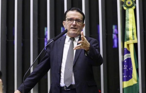 hélio costa falando e gesticulando na tribuna da câmara, com bandeira do brasil ao fundo