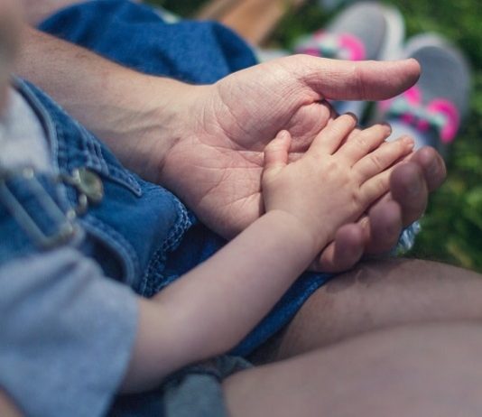 close em criança com a mãozinha sobre a mão de um homem adulto