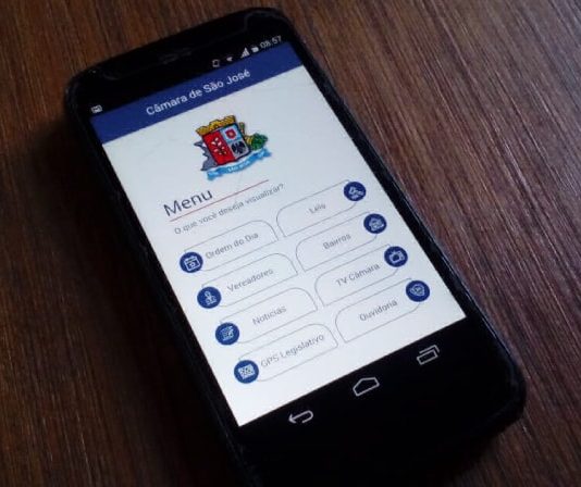 Aplicativo aproxima Câmara de São José da população durante a pandemia celular sobre mesa de madeira com o aplicativo da câmara de são josé aberto na tela