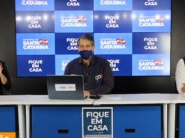 Santa Catarina tem 4.332 casos e 78 mortes por Covid-19 imagem da coletiva onde está, em uma bancada, o secretário ao centro, outro homem ao lado, e intérprete de libras do outro; painel de logos do governo ao fundo