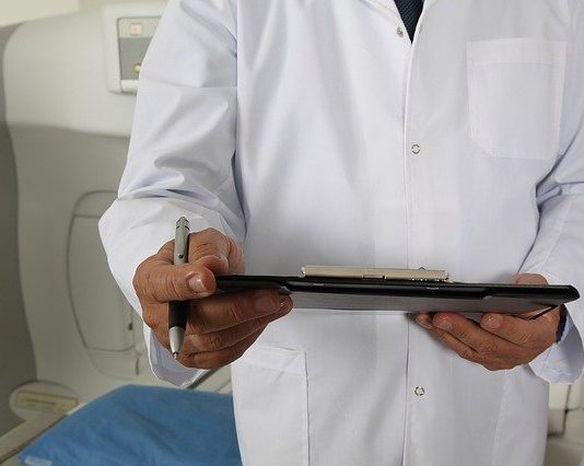 close em mãos de homem usando jaleco de médico e segurando prancheta com caneta