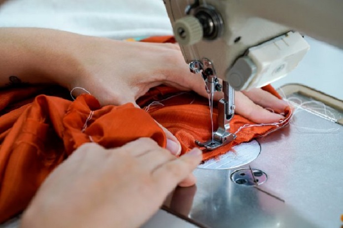 duas mãos operando uma máquina de costura