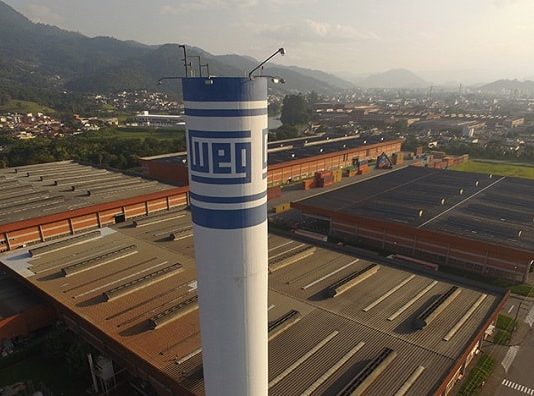 Governo de SC compra 500 respiradores da Weg por R$ 30 milhões Fábrica da Weg em Jaraguá do Sul vista em foto aérea com torre de caixa d'água com logo da empresa em primeiro plano, galpões em baixo, e cidade ao fundo