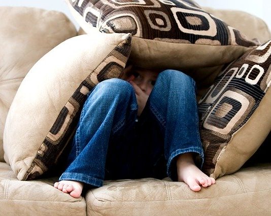 garoto se esconde debaixo de três almofadas em sofá