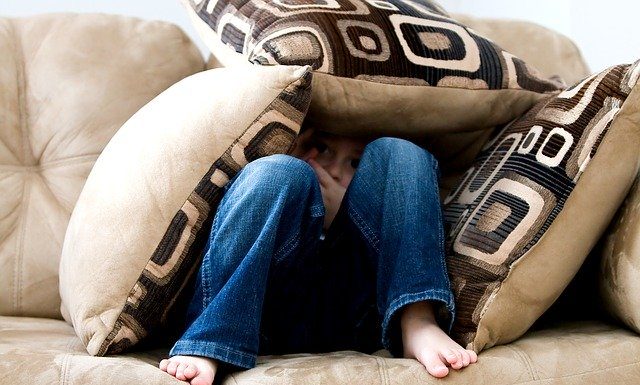 garoto se esconde debaixo de três almofadas em sofá