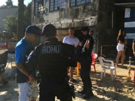 Guarda municipal interrompe festa em rancho na Praia do Curtume agente da guarda com inscrição ROMU nas costas fala com um homem na areia da praia e há pessoas e outros agentes em volta