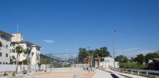 lajotas do piso colocadas em grande parte da área do parque e em outra chão de areia. prédios ao fundo