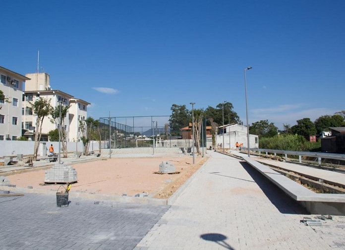 lajotas do piso colocadas em grande parte da área do parque e em outra chão de areia. prédios ao fundo