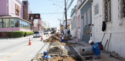 operários ao longo de buraco aberto em rua do centro histórico de são josé, carros desviando em meia pista