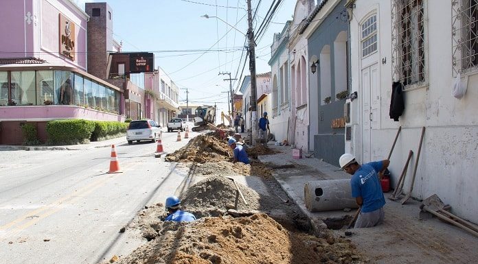 operários ao longo de buraco aberto em rua do centro histórico de são josé, carros desviando em meia pista