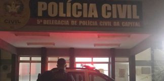 agente da guarda em frente à viatura estacionada em com luzes ligadas em frente à delegacia de polícia da trindade