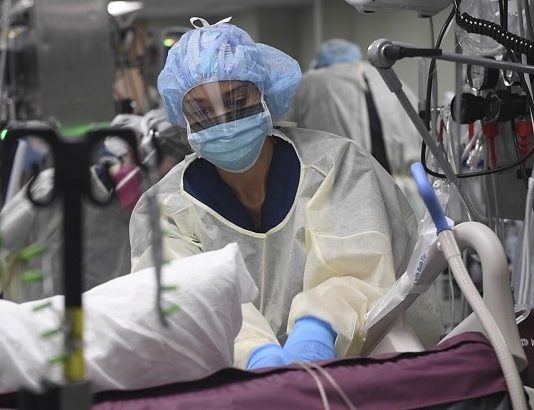 enfermeira usando equipamentos de proteção em todo o corpo faz massagem cardíaca em paciente em uti no meio de diversos aparelhos
