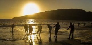 silhueta de pescadores puxando rede de arrasto na beira da praia do campeche, com ilha ao fundo e nascer do sol