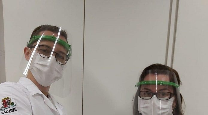 duas profissionais de saúde usando máscaras e faceshields e jalecos posando de braços cruzados para a foto