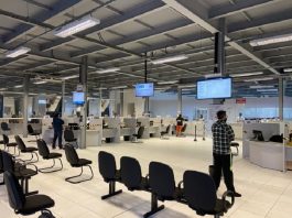 balcoes de atendimento do detran, com bancos na frente, dois homens em pé afastados, televisores