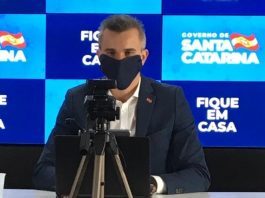 Deputados estaduais cobram demissão do secretário da Casa Civil borba usa máscara preta ao dar entrevista online; há uma câmera em tripé na sua frente e painel do governo ao fundo