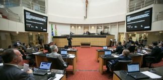 deputados sentados nas bancadas do plenário da alesc, com dois telões ao fundo e mesa diretora, com grande cruz no meio