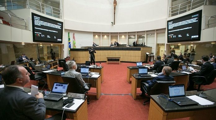 deputados sentados nas bancadas do plenário da alesc, com dois telões ao fundo e mesa diretora, com grande cruz no meio