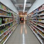 corredor de um supermercado cheio de produtos nas prateleiras e caixa ao fundo