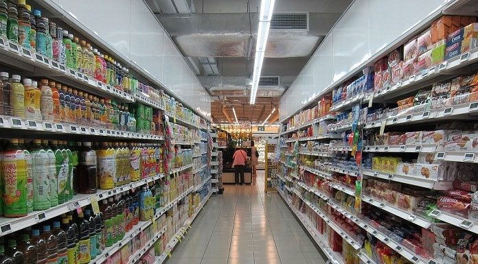 corredor de um supermercado cheio de produtos nas prateleiras e caixa ao fundo