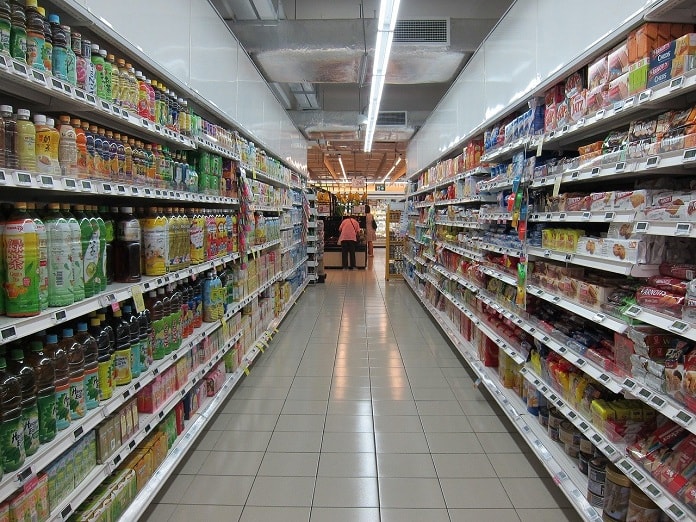 corredor de um supermercado cheio de produtos nas prateleiras e caixa ao fundo
