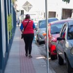 funcionária fiscal da zona azul andando em calçada ao lado de carros estacionados