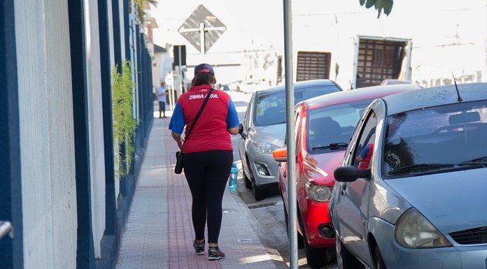 funcionária fiscal da zona azul andando em calçada ao lado de carros estacionados