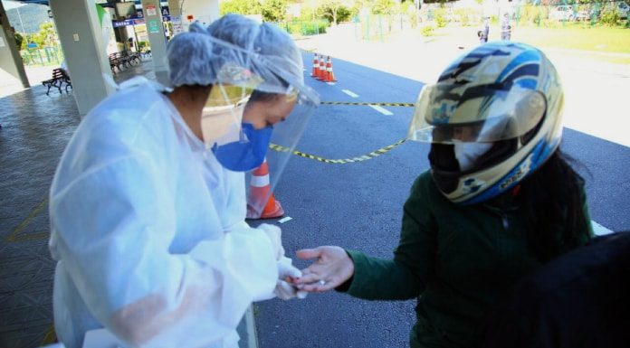 profissional de saúde trajada com equipamentos de segurança espeta dedo de mulher em garupa de moto usando capacete estendendo a mão em um terminal de ônibus