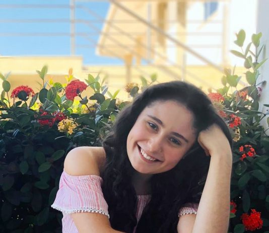 Cheiro de café Moça vestindo blusa rosa e calça azul, sentada na calçada com a mão esquerda no cabelo